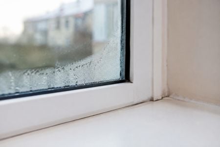 Fogged window with condensation along the glass and sill after humid storm conditions.