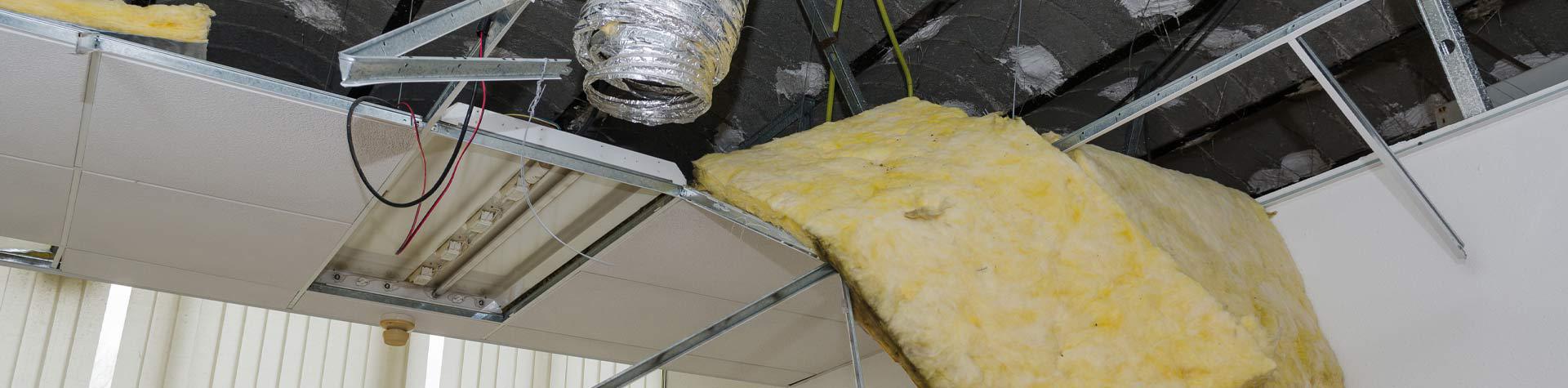 A ceiling with roof panels missing, exposing insulation, wires, and vents