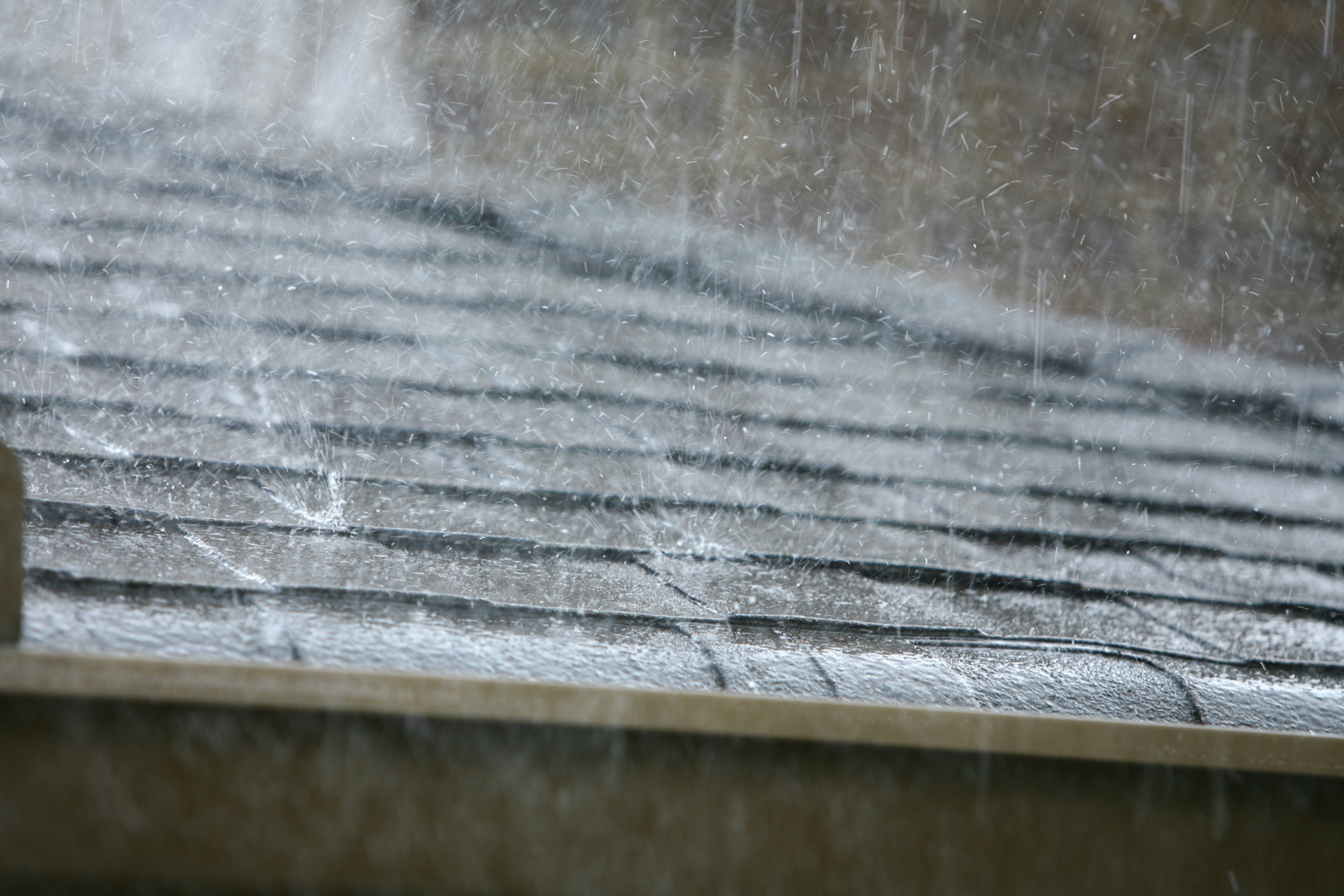 Heavy summer rain splashes across a residential roof, illustrating how storms can expose areas vulnerable to water intrusion.