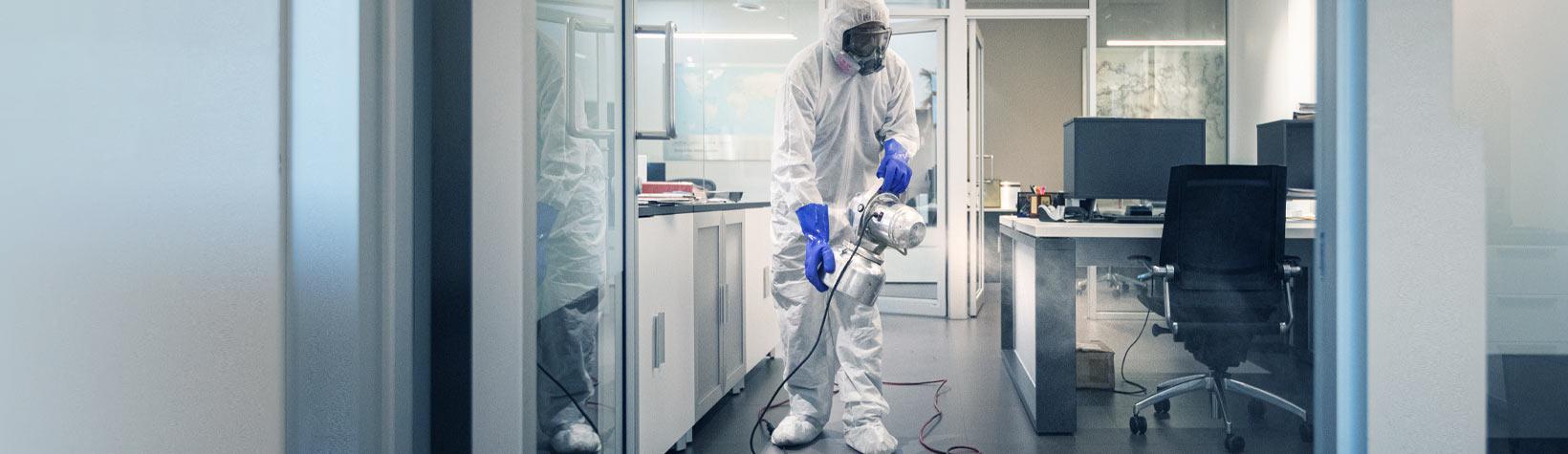 Sanitation worker in protective gear sanitizing an office interior